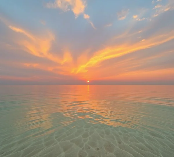 L’alba tinge il cielo di rosa e arancio, riflessa su acque calme. La sabbia dorata e il calore avvolgente creano un’atmosfera di pace totale
